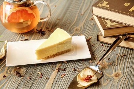 Una deliciosa rebanada de tarta de queso delicadamente colocada en un plato adyacente a una taza de té humeante, creando una deliciosa y reconfortante combinación de sabores.