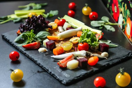 Une planche à découper noire présente un assortiment vibrant de légumes frais, prêts à être préparés et cuits.