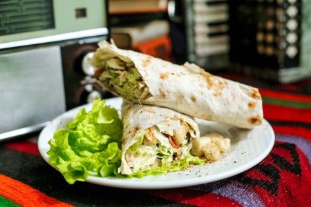 A burrito sits on a plate next to a microwave, accompanied by fresh lettuce.