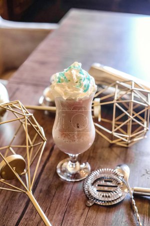 A close-up shot of a creamy drink topped with a generous swirl of whipped cream and colorful sprinkles, placed on a rustic wooden table.
