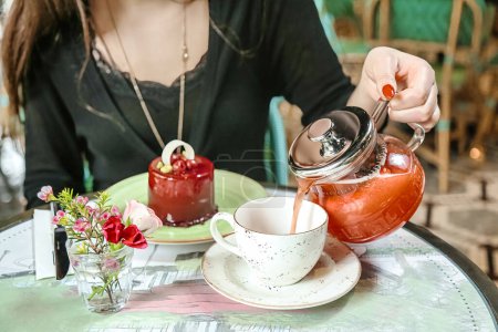 Eine Frau gießt Tee aus einer Teekanne in eine Tasse.