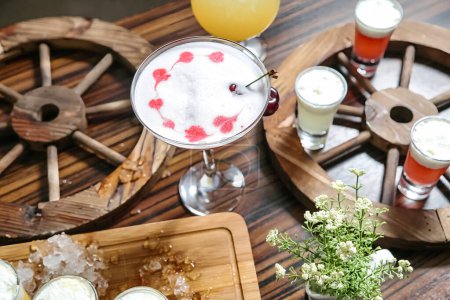 Se presenta una bandeja de madera con una selección de bebidas refrescantes, que incluyen agua, jugo, refrescos y cócteles, organizados cuidadosamente junto a otras opciones de bebidas..