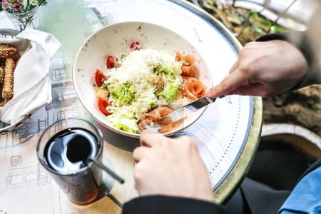Téléchargez les photos : Une personne s'assoit à une table et mange dans un bol de nourriture, affichant une activité typique à l'heure des repas. - en image libre de droit