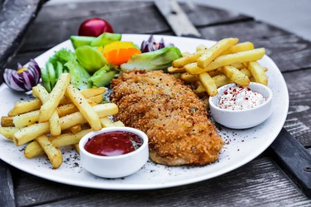 A white plate is filled with a savory arrangement of chicken and crispy french fries.