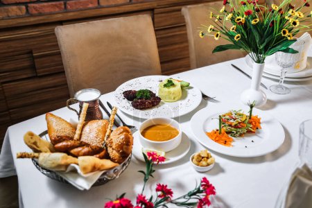 A white table is beautifully set with an enticing array of various dishes, including appetizers, main courses, and desserts.