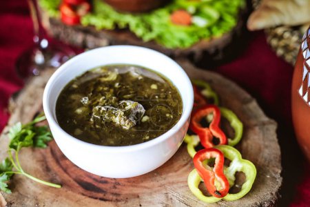 A wooden plate holds a bowl filled with vibrant green salsa.