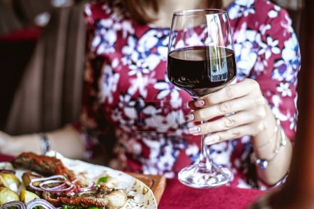 Una mujer está sentada en una mesa, con un plato de comida y una copa de vino delante de ella, disfrutando de su comida.