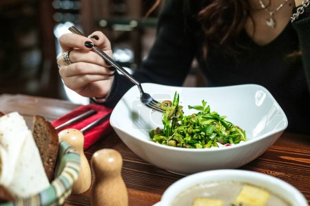 Una mujer se sienta en una mesa, usando un tenedor para comer de un tazón de comida.