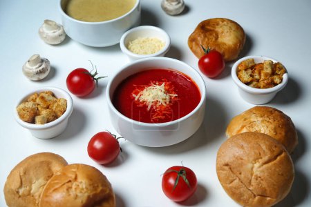 Une table blanche avec des bols assortis de soupe et des muffins fraîchement cuits.