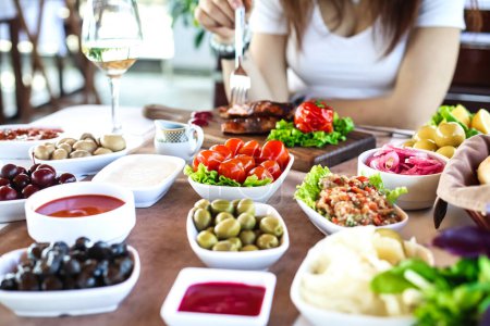 A table adorned with an array of food-filled bowls and accompanied by a solitary glass of wine.