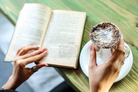 Une personne est assise dans un café extérieur, absorbée par un livre, tout en tenant une délicieuse pâtisserie.
