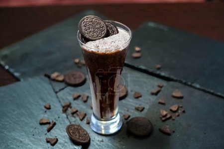 A chocolate milkshake in a glass with a delicious cookie placed on top.