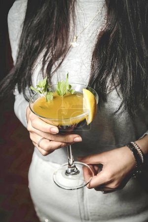 Eine Frau im lässigen Outfit hält ein Getränk in der Hand und amüsiert sich bei einer lebhaften gesellschaftlichen Zusammenkunft.
