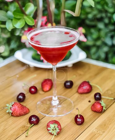 Un verre rempli d'un liquide frais et rafraîchissant et décoré de fraises mûres, placé sur une table.