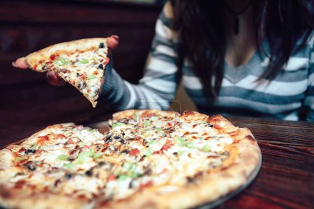 Una mujer sosteniendo una rebanada de pizza delante de su cara, mostrando su disfrute de la golosina cursi y delicioso.