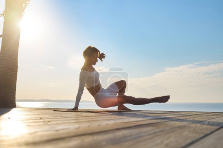 Photo for A woman is engaged in animal flow gymnastics outdoors near the sea on wooden floor. High quality photo - Royalty Free Image