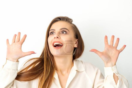 Foto de Retrato de una joven mujer caucásica con camisa blanca levanta las manos y ríe positivamente con la boca abierta mirando hacia arriba sobre un fondo blanco - Imagen libre de derechos