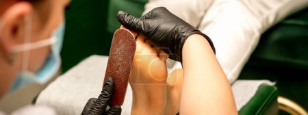 Photo for Pedicurist rubbing heel with a special grater on pedicure treatment in a beauty salon - Royalty Free Image