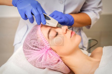 Téléchargez les photos : Jeune femme caucasienne recevant un nettoyage de la peau du visage par ultrasons équipement de cosmétologie visage dans un salon médical - en image libre de droit
