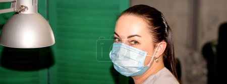 Téléchargez les photos : Jeune podiatre féminine avec un masque protecteur regardant la caméra dans sa clinique de podiatrie - en image libre de droit