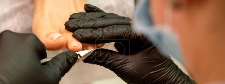 Photo for Professional pedicure. Pedicure master wearing latex gloves cuts female toenails in the beauty salon, closeup - Royalty Free Image