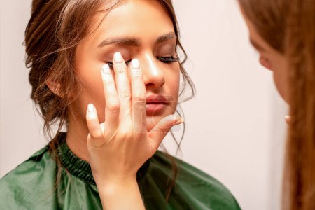 Photo for The hand of a makeup artist applies eye shadow on the eyelid of a young Caucasian woman with fingers in a beauty salon - Royalty Free Image