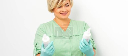 Photo for Cosmetics creams and skin care products in the hands of the female beautician smiling and standing over the white wall background - Royalty Free Image