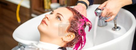 Téléchargez les photos : Laver les cheveux teints des femmes. Une jeune femme caucasienne se fait laver les cheveux dans un salon de beauté. Coiffeur professionnel lave la peinture de couleur rose sur les cheveux d'un client - en image libre de droit