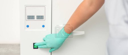 Photo for Beautician in protective gloves starts the machine for disinfection of tools before the medical procedure - Royalty Free Image