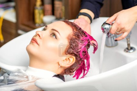 Photo for Washing dyed female hair. A young caucasian woman having her hair washed in a beauty salon. Professional hairdresser washes pink color paint off of a customer's hair - Royalty Free Image