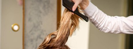 Photo for Professional hair care. Young female blonde with long hair receiving hairstyling in a beauty salon - Royalty Free Image