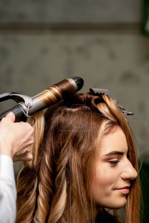 Photo for The female hairdresser is curling hair for a brown-haired young caucasian woman in a beauty salon - Royalty Free Image