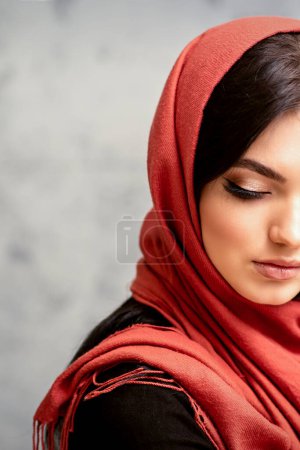 Photo for The fashionable young woman. Portrait of the beautiful female model with long hair and makeup with eyelash extensions in a red scarf. Beauty young caucasian woman on the background of a gray wall - Royalty Free Image