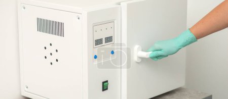 Photo for Beautician in protective gloves close the door of the machine for disinfection of tools before the medical procedures - Royalty Free Image