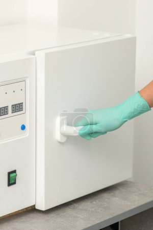 Photo for Beautician in protective gloves close the door of the machine for disinfection of tools before the medical procedures - Royalty Free Image