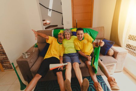 Photo for Group of Soccer Fans Celebrating the cup in the living room watching football game. Multi Ethnics Family Cheering for Brazil to be Champion. - Royalty Free Image