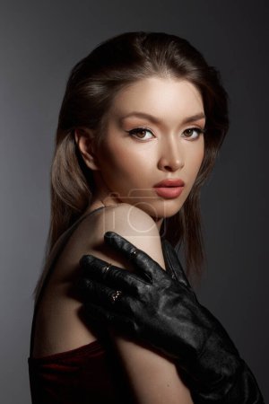 Captivating gaze of a woman in a burgundy dress, accented by elegant black gloves and subtle jewelry