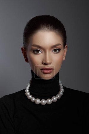 Elegant female model in a black turtleneck and lustrous pearl necklace showcases a blend of classic beauty with modern sophistication