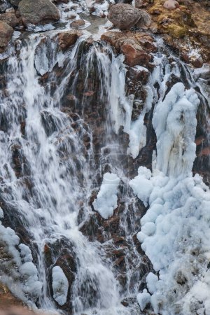 Chilly cascade waterfall, where water rushes over icy rocks, intertwining liquid flow with frozen formations