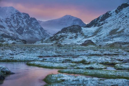 Twilight descends on a tranquil mountain valley with snow-capped peaks and a gentle river