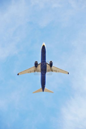Avión comercial capturado desde abajo mientras sube al vasto cielo azul, mostrando su vientre inferior y motores a reacción