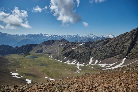 Panoramablick von einem Berggipfel mit einer Reihe von schneebedeckten Gipfeln, einem klaren blauen Himmel über dem Kopf und einem ruhigen Bergsee