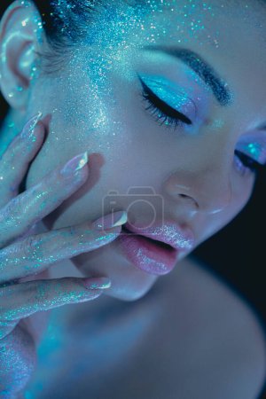 Foto de Maquillaje de belleza de brillo de tema cósmico de mujer, resaltando ojos y mejillas bajo iluminación azul - Imagen libre de derechos