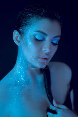 Mujer con llamativo maquillaje de belleza azul con purpurina aplicada en su cuerpo