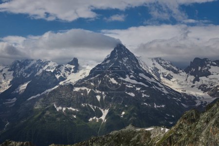 Towering mountain peak, snow capped and surrounded by rugged terrain under a dramatic sky