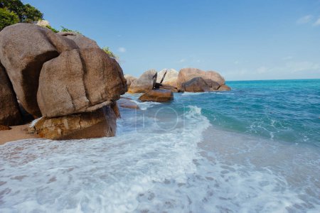 Rivage de plage avec de grandes roches éparpillées dans l'eau, créant un paysage marin unique et accidenté