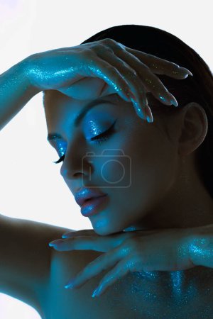 Beauty Woman posiert mit schimmerndem, blau getöntem Make-up, das durch kühles Studiolicht hervorgehoben wird