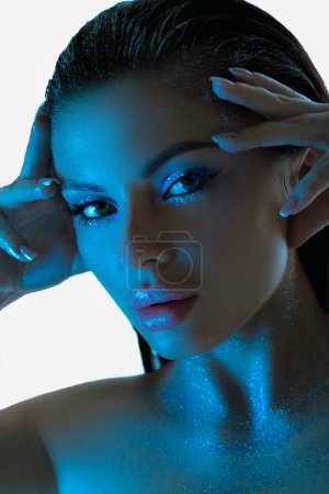 Beauty woman poses with glowing blue lights accentuating her eyes and complexion against a dark background