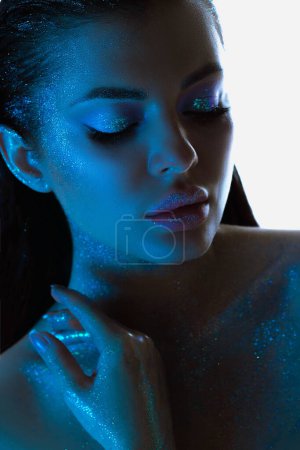 Womans profile glows with sparkling skin, highlighted by blue tones makeup, exuding a calm and mystical aura