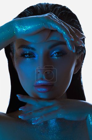 Maquillaje cosmético de mujer de belleza, brillo que adorna su piel, bajo una tenue iluminación azul